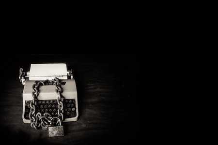 Information censorship concept - Typewriter locked with a chain and padlock on a black backgroundの写真素材