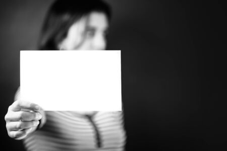 Serious young adult woman holding a blank sign - Her face is out of focusの写真素材