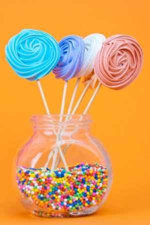 Colorful and sweet meringue lollipops on a bright orange backgroundの写真素材