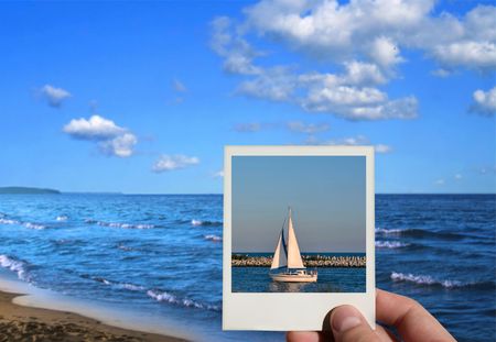 hand holding a holiday photo, beautiful seashore in background, photo inside is my propertyの写真素材