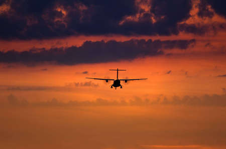 Sunset scene with silhouette of a landing planeの写真素材