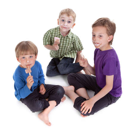 three kids eating ice lolly on white backgroundの写真素材