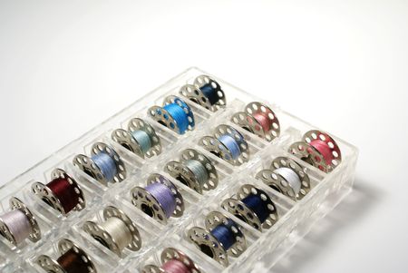 a clear tray filled with different colored sewing bobbinsの写真素材