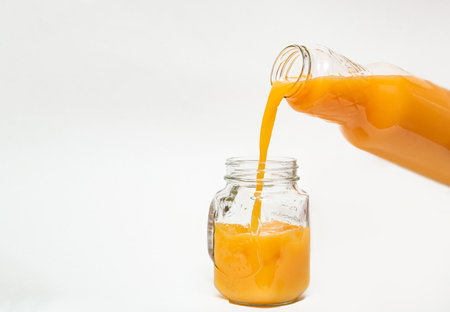 Orange juice pouring from a bottle into a glass, isolated on a white background, healthy citrus drink with copy spaceの写真素材