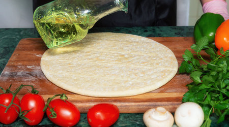 The chef prepares traditional pizza dough on a wooden Board. It uses olive oil or sauce. There are fragrant spices, vegetables and fresh herbs nearby.の写真素材