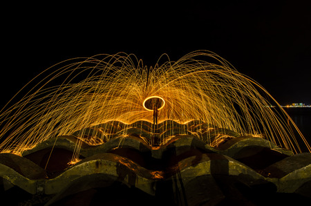 Showers of glowing sparks from spinning steel wool by the seashore at night.