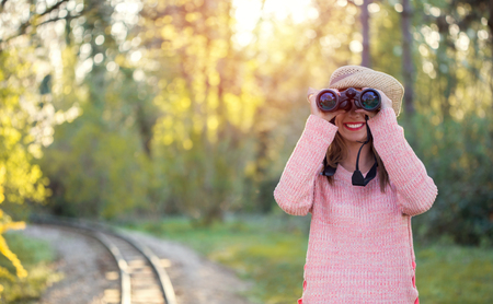 Beautiful young woman looking through binoculars in the forest with a railway next to herの写真素材
