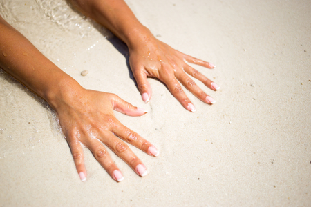 Womens hands on the beach sand at the oceanの写真素材