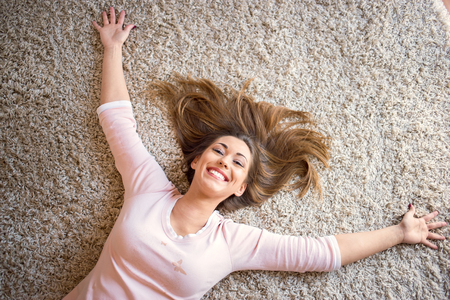 Beautiful happy woman lying on a carpet in the living roomの写真素材