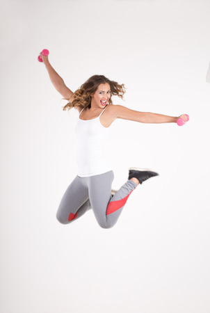 Fitness woman jumping in the air with dumbbells while smiling and looking at the cameraの写真素材