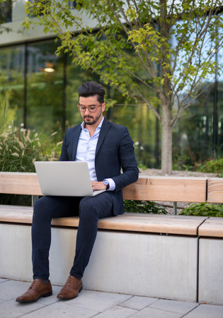Handsome young businessman working outside on his laptop daytimeの写真素材
