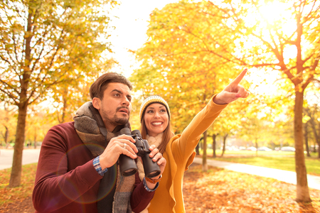 Happy young couple exploring in autumn at the park with binocularsの写真素材