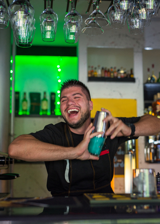 Handsome young barman mixing a blue cocktail in a bar