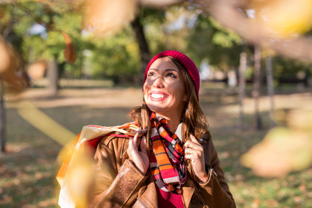 Beautiful young woman walking in a park in autumn after shopping while smilingの写真素材