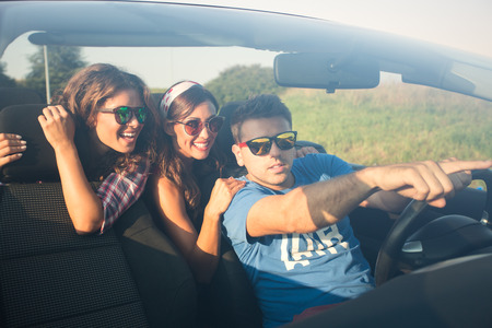 Three friends driving around in a convertible exploring pointing at something