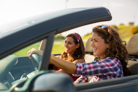 Two young beautiful girls driving in a convertible while smiling