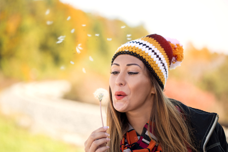 Beautiful young woman blowing dandelion outside in a fieldの写真素材