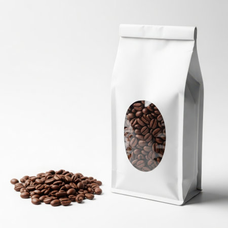 A white bag with a transparent oval window showcasing coffee beans, accompanied by a small pile of coffee beans on a plain white background.の素材