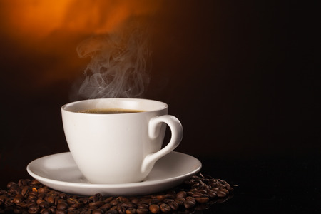 cup of coffee and coffee beans over dark background