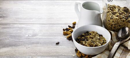 Muesli in the bowl, jar and jug with milk on wooden table.  Healthy breakfast composition. Place for...