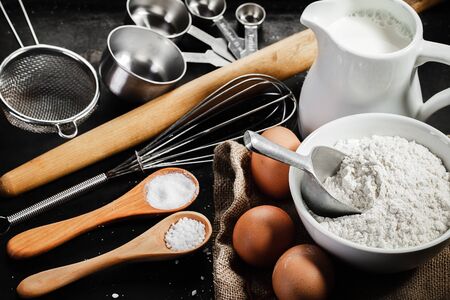 dough ingredients and  kitchen utensils on dark background