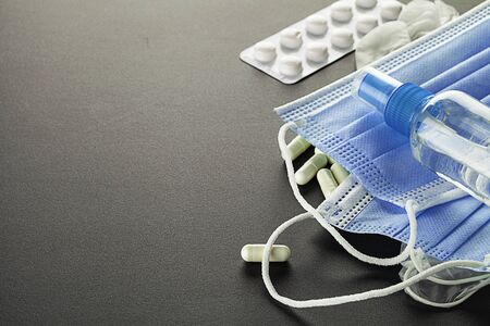 Medical surgical mask, sanitizer gel, lab gloves, pills and tablets  lying on the table. Virus...