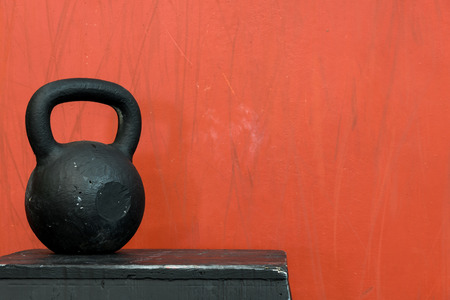 Black kettle bell on a black jump box, against a red wallの写真素材