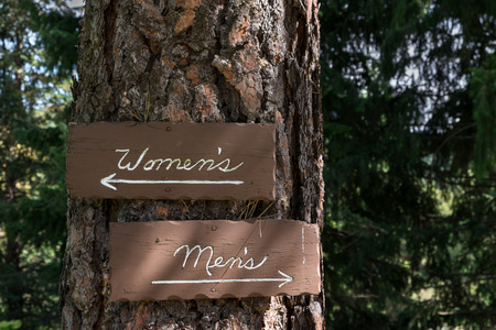 Wood outhouse signs, womenâs and menâs, on a treeの写真素材