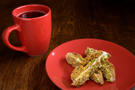 Homemade biscotti on a red plate, with a red coffee cup on a wood tableの写真素材