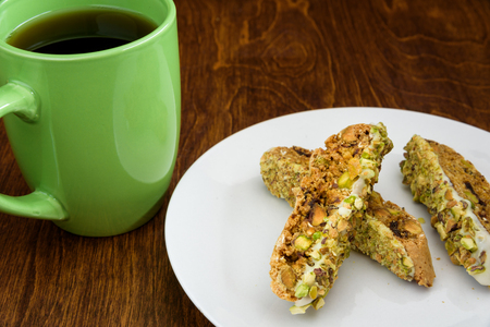 Homemade biscotti on a white plate, with a green coffee cup on a wood tableの写真素材