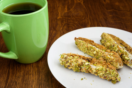 Homemade biscotti on a white plate, with a green coffee cup on a wood tableの写真素材