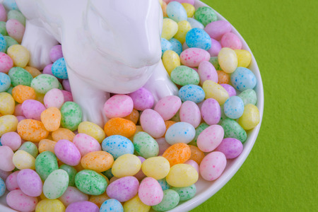 Close up of jelly beans and a white ceramic bunny on a white cake plate on a green fabric backgroundの写真素材