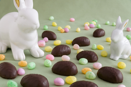 Two white ceramic Easter bunnies in a field of chocolate covered marshmallow eggs and colorful jelly beansの写真素材