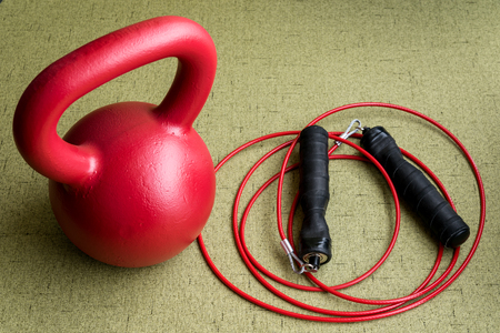 Red kettle bell and red jump rope on a light green backgroundの写真素材