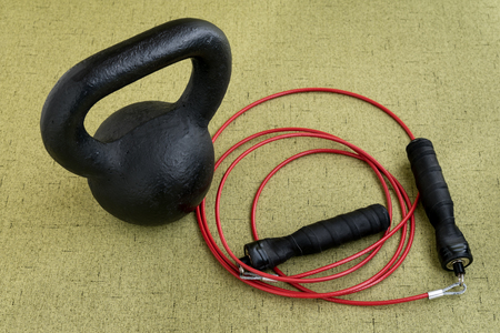 Black kettle bell and red jump rope on a light green backgroundの写真素材
