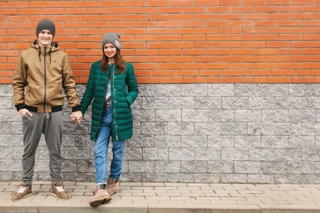 Young couple smiling and holding their hands. Casual clothes, urban, brick background. Copyspaceの写真素材