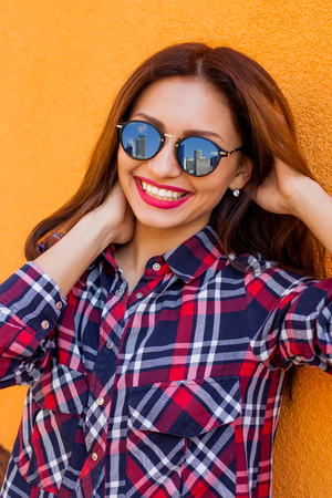 Closeup portrait of beautiful women with perfect make-up and sunglasses with reflection, smiling. Concept target, dream. Archive a goal. Orange backgroundの写真素材