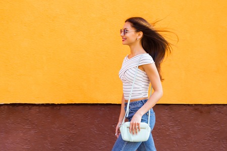 Portrait of stylish woman in sunglasses with make-up and flying hairs. Urban. Orange backgroundの写真素材