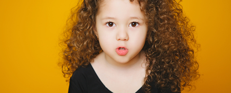Little curly girl kissing in studio on orange background. Copy-text. isolated