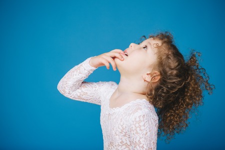 little curly girl looking up on blue background. Copy-space. Isolatedの写真素材