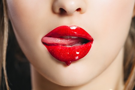 Red lip gloss. Closeup mouth with tongue. Saturated color. Studioの写真素材