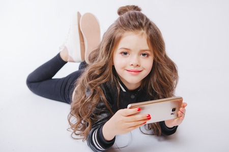 Portrait of cute little girl laying on the floor with telephone. Playing games. Studioの写真素材