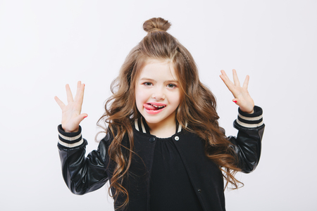 Portrait of little hipster girl in bomber jacket showing tongue. Posing. Curly modern hairstyle. Smiling. Studioの写真素材