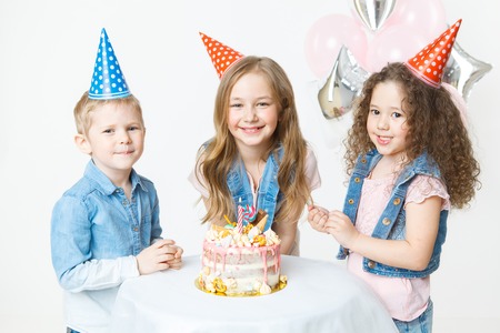 Group of kids in festive cap sit near birthday cake and smile. Celebration. Birthday party