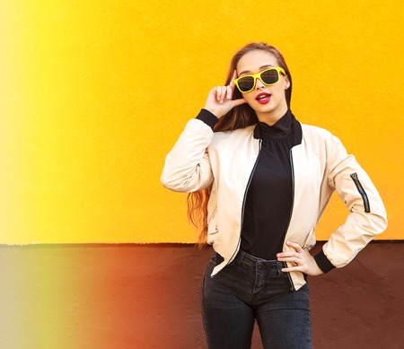 Young hipster girl in yellow sunglasses smiling on orange wall. Urban style. Vintage.の写真素材