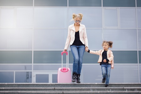 Mother and daughter with pink luggage in pink jacket against the airport. Outdoorの写真素材