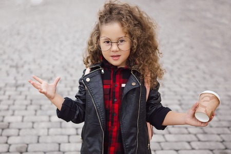Portrait of little curly hipster girl in glasses with coffee. Urban style. Autumn. Outdoor. Copy-spaceの写真素材