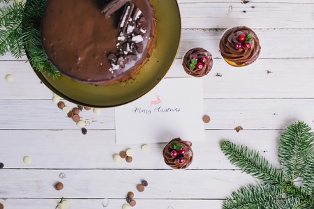 Dark chocolate cake with cookies and cupcakes berries on white wooden background. Lettering. Postcard. Congratulationsの写真素材