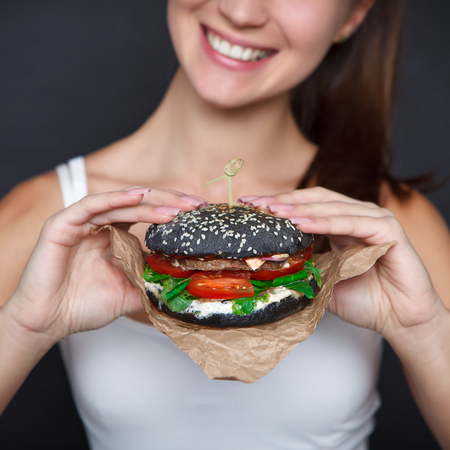 Close-up black burger in the woman hands. Nail design. Concept unhealthy, fast foodの写真素材