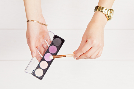 Flat lay with hands holding visage brush and eye shadows. Accessories and decorations on the white wooden background. Indoorの写真素材